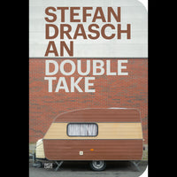 Buchcover von Stefan Draschan, An Double Take. Ein alter, braun-beiger Wohnwagen steht vor einer Backsteinmauer mit Betonverkleidung. Der Autorenname steht in Braun auf dem Beton, der Titel in Weiß auf Ziegel und Beton.