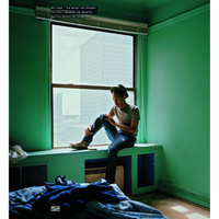 Ein junger Mann mit Hut sitzt nachdenklich auf der Fensterbank eines Zimmers mit leuchtend grünen Wänden. Durch das große Fenster hinter ihm ist die Fassade eines Hochhauses zu sehen. Im Vordergrund liegt unordentliche Bettwäsche auf einem Bett.