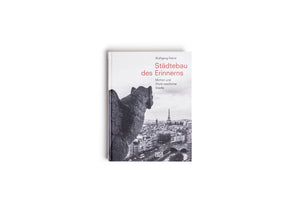 Ein Foto des Buches Städtebau des Erinnerns von Wolfgang Pehnt. Das Buchcover zeigt eine Schwarz-Weiß-Fotografie einer steinernen Chimäre, die von oben auf Paris blickt. Im Hintergrund ist die Silhouette der Stadt mit dem Eiffelturm zu sehen. Das Buch liegt auf einer weißen Oberfläche.