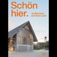 Das Buchcover von Schön hier. Architektur auf dem Land zeigt ein modernes Gebäude aus Holz und Beton, das bei Dämmerung auf einem Dorfplatz steht. Im Hintergrund ist ein Kirchturm zu sehen.