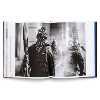 Ein aufgeschlagenes Buch mit einer Schwarz-Weiß-Fotografie des Sturms auf das US-Kapitol. Im Vordergrund steht ein Mann mit einer Trump 2020 Mütze und einem Bandana, der eine Flagge hält, während im rauchigen Hintergrund weitere Personen zu sehen sind, eine davon mit einer Gasmaske.