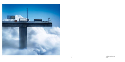 Eine surreale Szene, die einen Betonsteg zeigt, der hoch über einem Meer aus weißen Wolken unter einem strahlend blauen Himmel schwebt. Auf dem Steg, der an eine Haltestelle oder ein Flugsteig erinnert, stehen eine leere Bank, ein Koffer, ein Schild und ein Laternenpfahl.