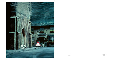 Eine surreale, zweigeteilte Ansicht einer überfluteten Straße, die wie ein Diorama wirkt. Die untere Hälfte zeigt eine Straße mit einem Steingebäude, dessen Tür mit Sandsäcken geschützt ist, und einem Warnschild mit der Aufschrift Flood. Die obere Hälfte zeigt die unruhige Wasseroberfläche von unten.