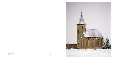 Fotografie eines Dioramas einer kleinen Kirche in einer verschneiten Landschaft. Das Gebäude mit spitzem Turm und das Dach sind schneebedeckt, daneben stehen ein Baum und ein Auto im Schnee.