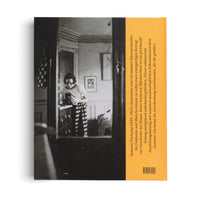 Die Rückseite eines Buches mit einem großen Schwarz-Weiß-Foto und einem gelben Textstreifen rechts. Das Foto zeigt eine Frau in gestreifter Hose, die in einem Zimmer über eine Kommode gebeugt ist.